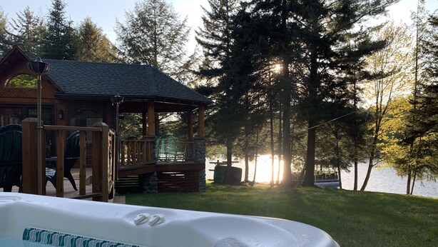 A hot tub on a wooden deck with a view of a lake and trees.