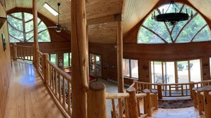 A wooden cabin with a central staircase, large windows, and a ceiling fan.