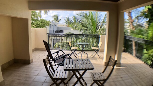 A covered outdoor patio with a wooden table and chairs, a small round table, and a black metal railing. - Huge House in Fort Lauderdale - 819 (Fort Lauderdale)