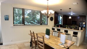 A dining area with a wooden table and chairs, a chandelier, and a view of the kitchen through a window with blinds. - Huge House in Fort Lauderdale - 819 (Fort Lauderdale)