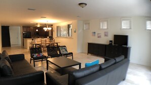 A modern living room with a black leather sofa, a dining area with wooden chairs and a table, a kitchen with dark cabinets, and a flat-screen TV mounted on the wall. - Huge House in Fort Lauderdale -  821 (Fort Lauderdale)