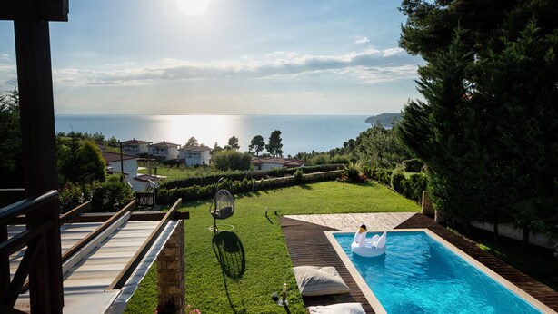 Ein Schwimmbecken mit einer Schwane als Schwimmpflege, einer Holzterrasse und Blick aufs Meer.