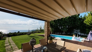 Eine Terrasse im Freien mit Tisch und Stühlen, ein Schwimmbad und Blick auf das Meer.