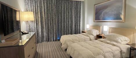 A hotel room with a large bed, a ceiling fan, a TV, a desk, and a painting on the wall.