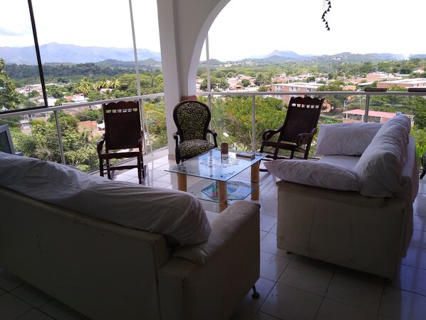 Un balcón con dos sillas y una mesa, con vistas panorámicas a un pueblo y montañas.