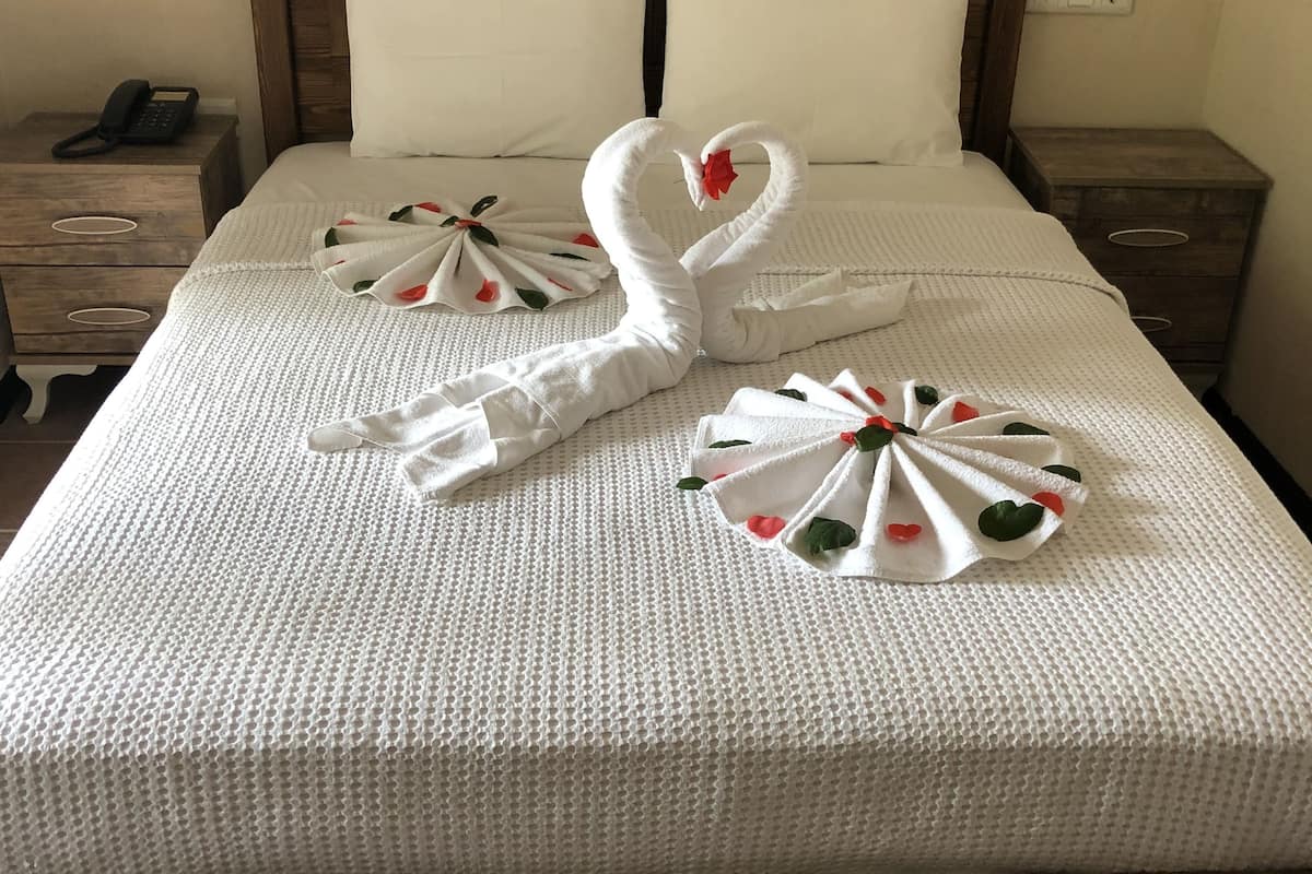 Ein ordentlich bezogenes Bett mit einem hölzernen Kopfteil, zwei Kissen und zwei dekorative Handtücher in Form von Schwänen mit roten Blumen.