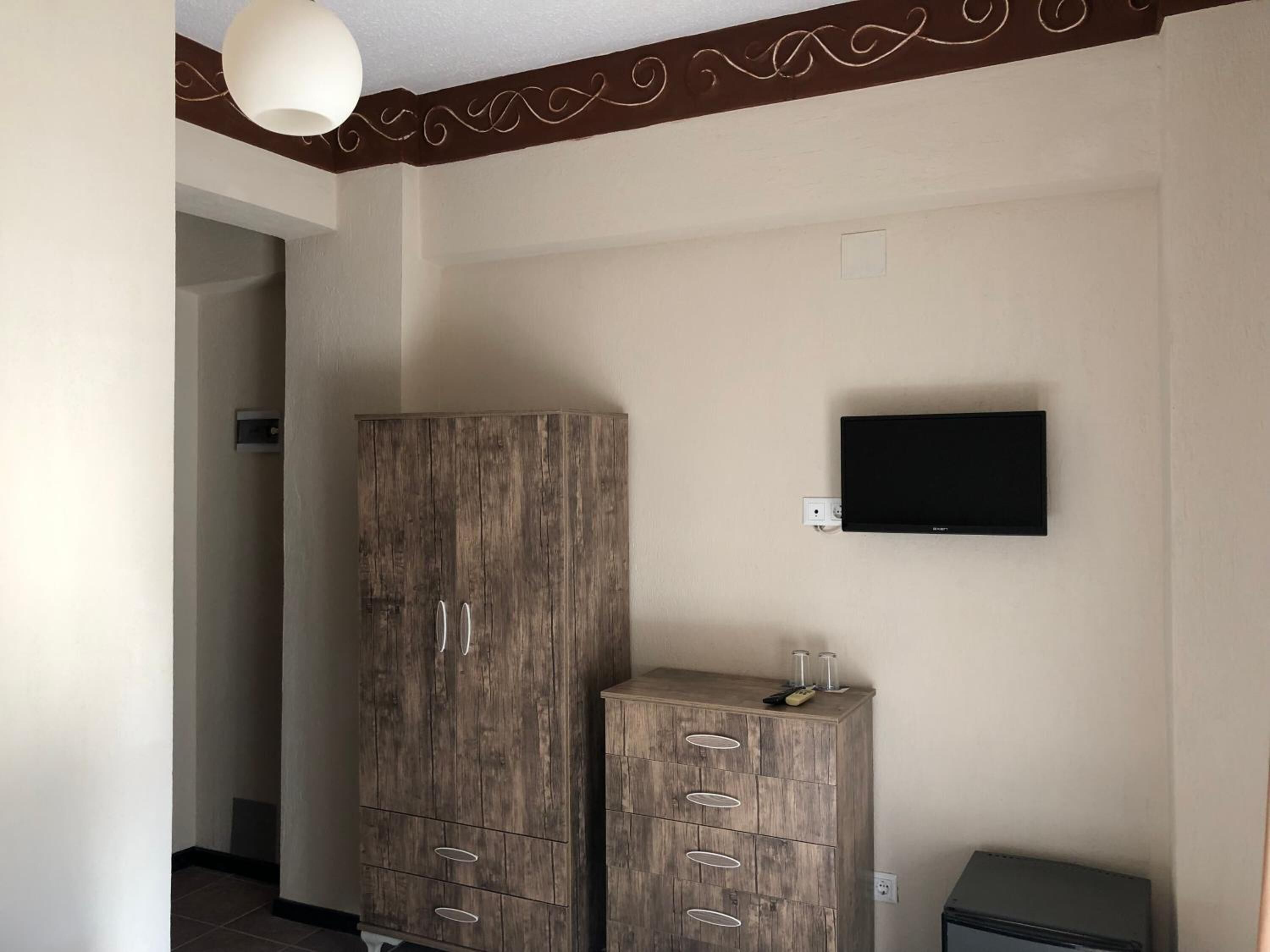 A room with a large wardrobe, a television mounted on the wall, and a small cabinet with drawers.