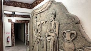 A hallway with a stone relief sculpture of two figures, a fire extinguisher, and a sign reading "Yangun 112". - Nehir Suit Hotel (Ortaca)