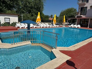 Una piscina con borde de azulejos, rodeada de sillas de descanso y sombrillas.