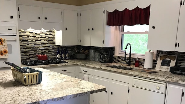 A kitchen with white cabinets, a granite countertop, a red kettle, and a window with a red valance. - OUR HOME ...AWAY FROM HOME (Laurel Springs)