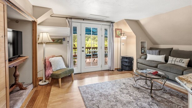 A cozy living room with a television, a sofa, a glass coffee table, and a view through a glass door to an outdoor patio. - Night Owl - Murphys Vacation Rentals (Murphys)