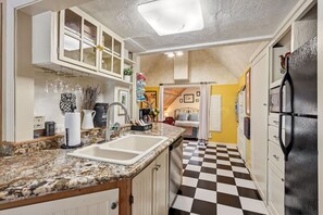 A kitchen with a checkered floor, a sink, a refrigerator, and a dining area with a bed. - Night Owl - Murphys Vacation Rentals (Murphys)