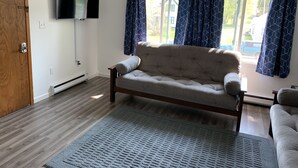 Una sala de estar con un sofá, un televisor montado en la pared y una ventana con cortinas.