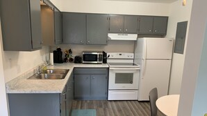 Una cocina compacta con armarios grises, un lavamanos de acero inoxidable, un microondas, un horno y un refrigerador.