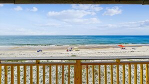Blick auf einen Strand von einer Holzterrasse aus, der Himmel ist klar.