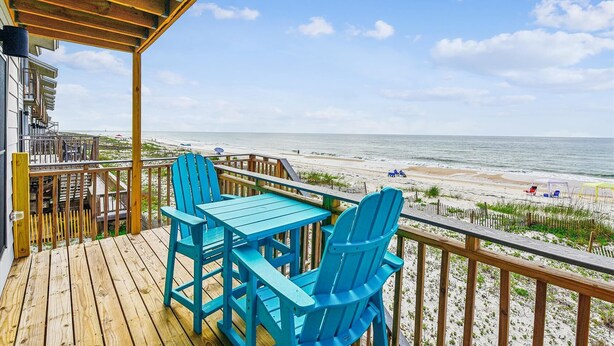 Eine Holzterrasse mit blauen Stühlen und einem Tisch mit Blick auf einen Strand.