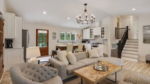 Ein geräumiges Wohnzimmer mit grauem Sofa, einem Holztisch und einem Essbereich, im Hintergrund befindet sich eine Küche.