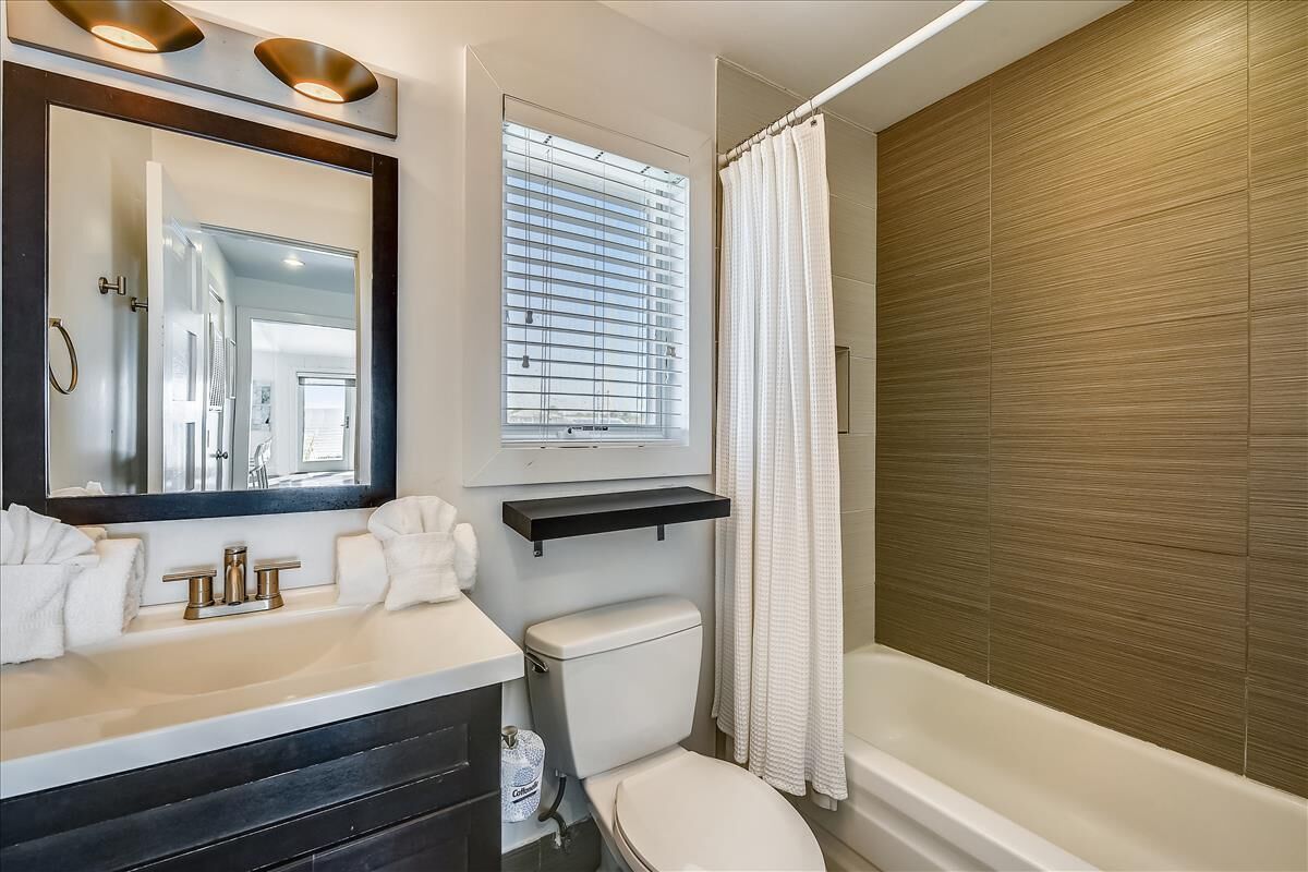 Ein modernes Badezimmer mit einem weißen Waschbecken, einer Toilette, einer Badewanne und einem Fenster mit Jalousien.