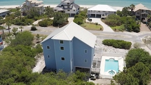 Un quartier résidentiel situé sur la côte, avec plusieurs maisons, une piscine et une plage en arrière-plan.