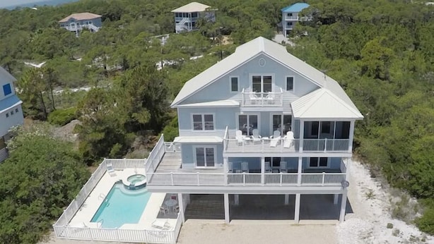 Une grande maison à deux étages avec une piscine, entourée d’arbres et d’autres maisons.