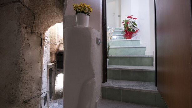 A narrow hallway with a white wall and a door leading to a staircase with green tiles. - Alfieri rooms - flat Conchiglia (Atrani)