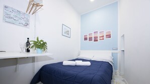 A neatly made bed with a blue bedspread and white pillows, a small plant on a white shelf, a framed picture, and a wall with three sunset images. - Alfieri rooms - flat Conchiglia (Atrani)