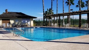 A swimming pool with a covered area, lounge chairs, and a building with a sign.