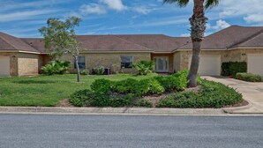 A two-story house with a front yard, a palm tree, and a driveway.