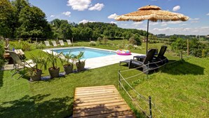 Uma área de piscina com deck de madeira, espreguiçadeiras e um guarda-sol de palha.