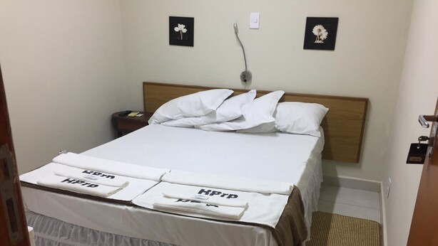 Una cama bien hecha con ropa blanca y falda cubrecolchón. Hay dos mesitas de noche con lámparas, y una pequeña alfombra en el suelo.
