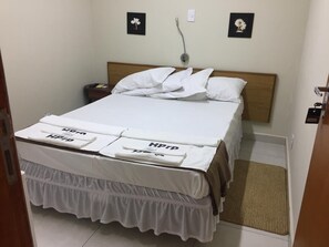 Un letto rifatto con lenzuola bianche e coprimaterasso a balze. Due comodini con lampade e un piccolo tappeto sul pavimento.
