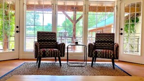 A room with two patterned chairs, a small table, and a large window with a view of a tree and a building. - Family-Friendly 4BR Ranch Home Near Sedona w/ Porch, Fire Pit & Private Spa (Cottonwood)