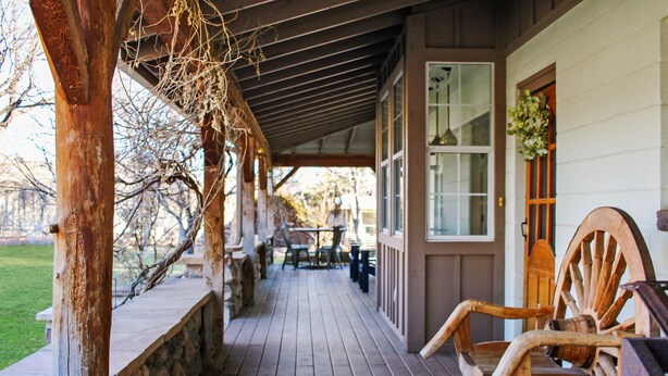 A wooden porch with a stone bench, wooden chairs, and a table. - Family-Friendly 4BR Ranch Home Near Sedona w/ Porch, Fire Pit & Private Spa (Cottonwood)