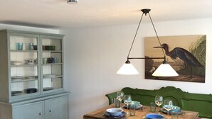 Un comedor con mesa de madera preparada para dos comensales, un banco tapizado de verde y un aparador con puertas de cristal.