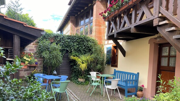 Un patio con un banco azul, una mesa con sillas y plantas en macetas.