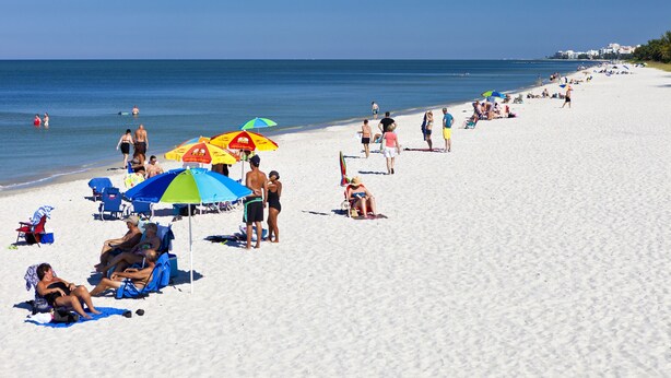 Una playa con gente tomando el sol y nadando, sombrillas y sillas de playa.