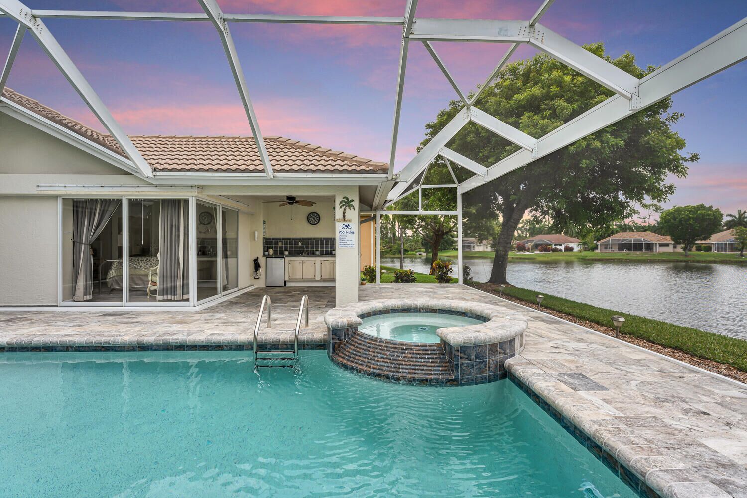 A swimming pool with a hot tub, a covered patio, and a view of a lake.
