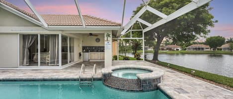 A swimming pool with a hot tub, a covered patio, and a view of a lake.