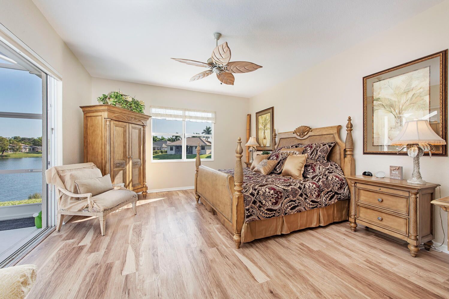 A bedroom with a large bed, a wooden wardrobe, a chair, a nightstand, and a view of a lake.