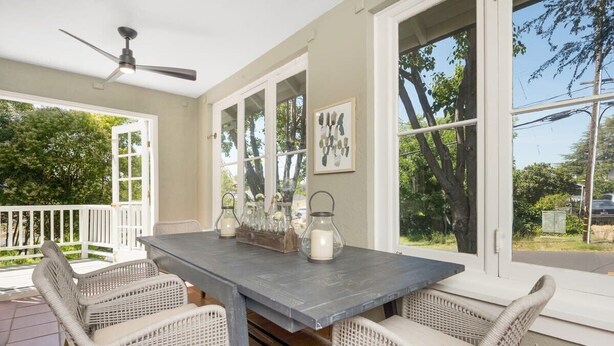 A dining area with a table and wicker chairs, large windows, and a ceiling fan. - The Oxbow House - Designer 3BD/2BA Home (Napa)