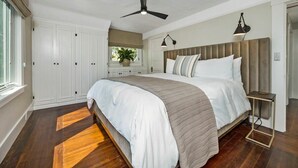 A bedroom with a large bed, a ceiling fan, a bedside table, and a window with a view of the outdoors. - The Oxbow House - Designer 3BD/2BA Home (Napa)