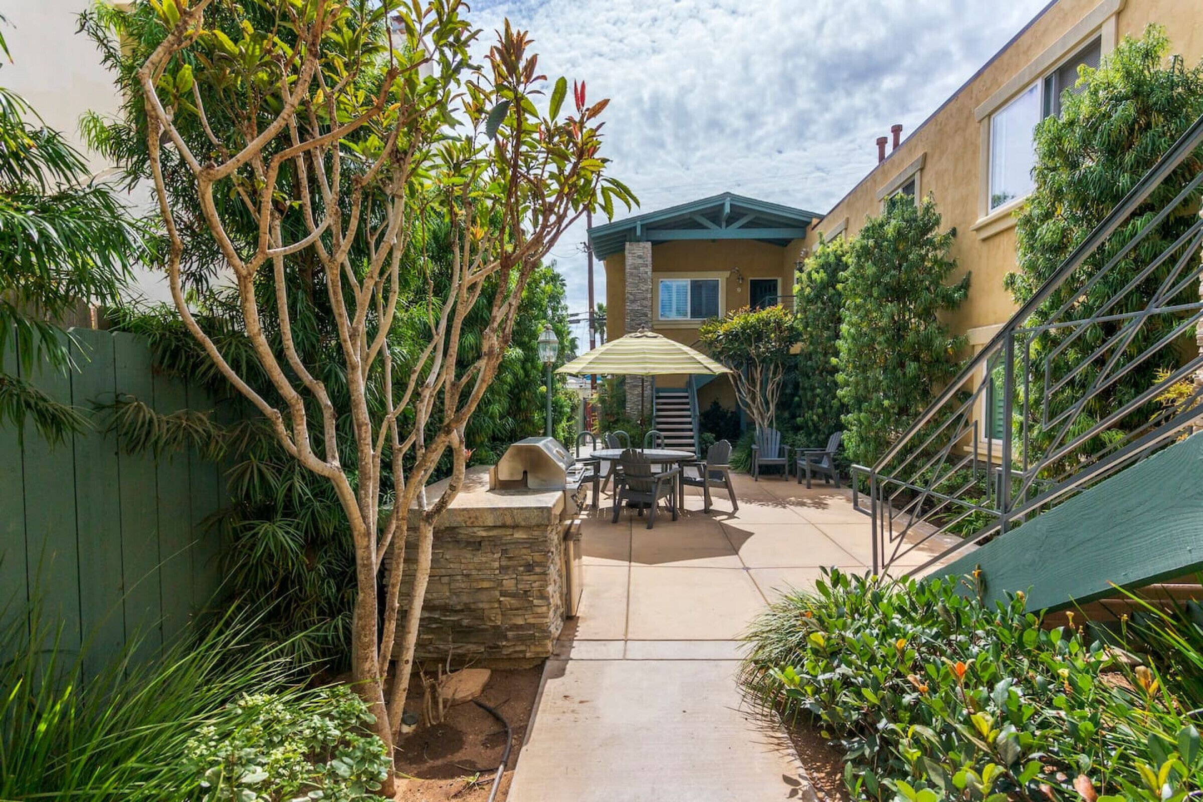 A patio area with a barbecue grill, outdoor seating, and a staircase leading to a building.
