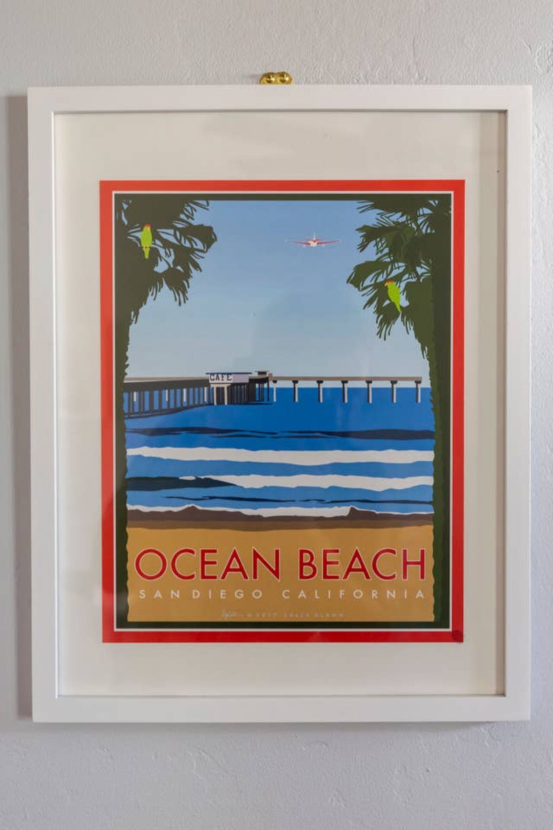 A framed picture of Ocean Beach in San Diego, California, featuring a pier, palm trees, and a clear blue sky.