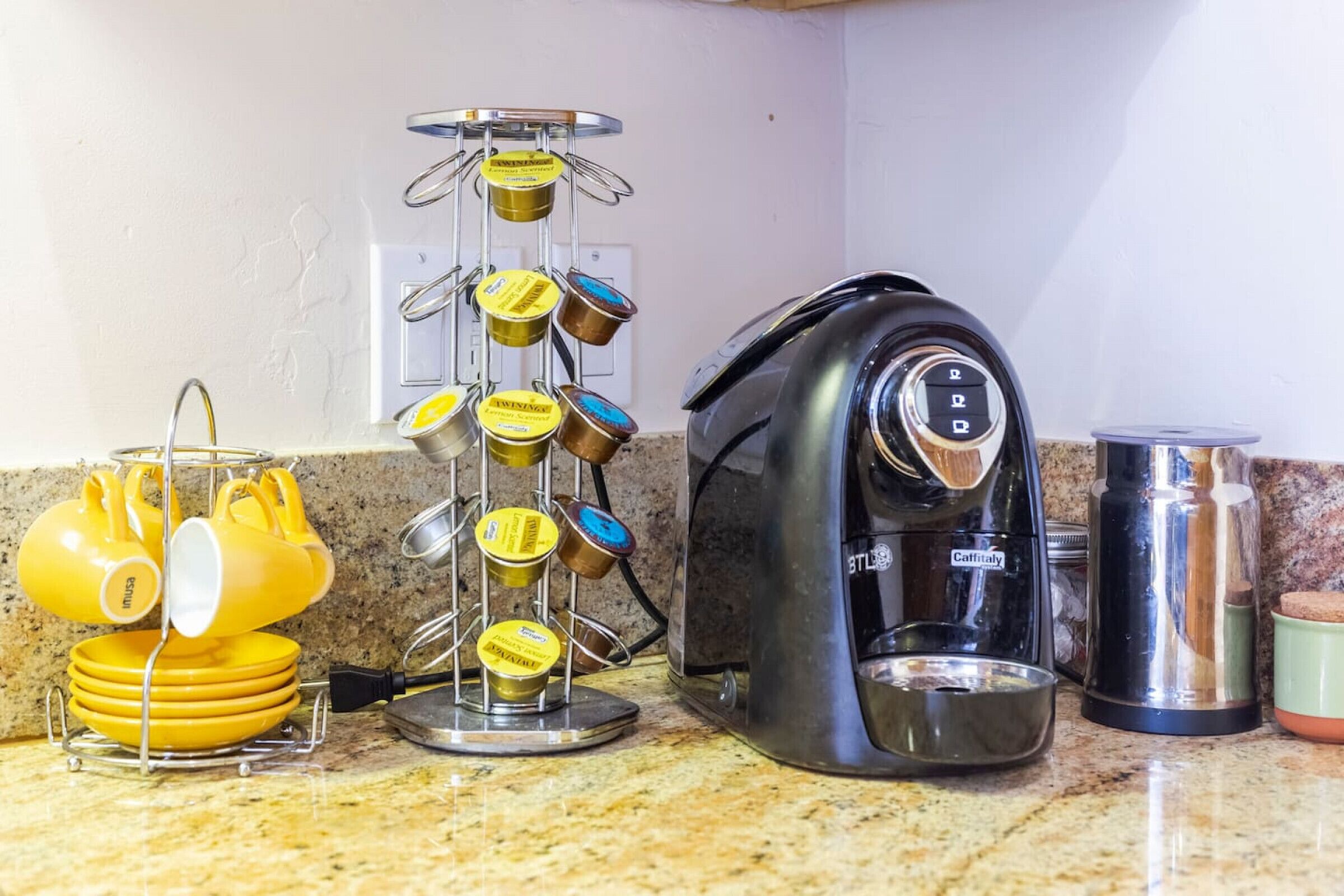 A kitchen counter with a coffee maker, a dish rack with yellow and brown dishes, and a metal container.