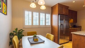 Una cocina moderna con un refrigerador de acero inoxidable, armarios de madera y un comedor con una mesa blanca y sillas amarillas.