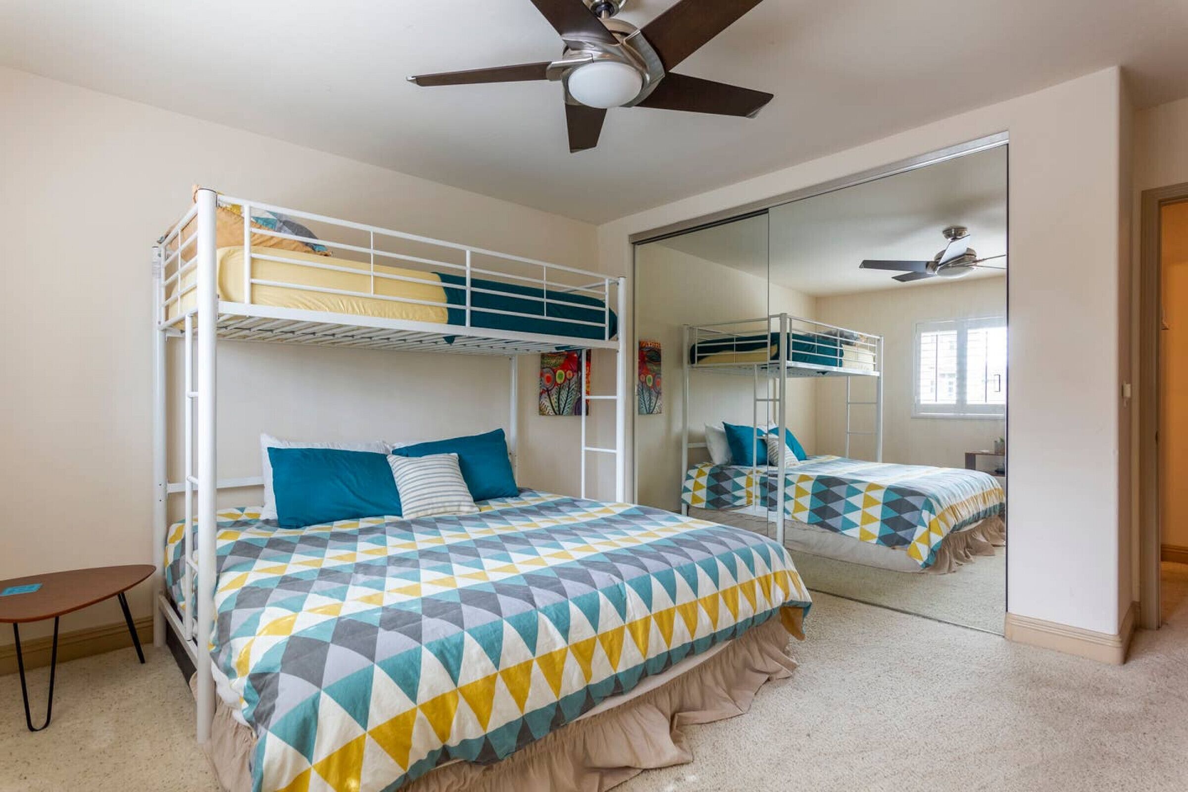 A bedroom with bunk beds, a ceiling fan, a mirror, and a small table.
