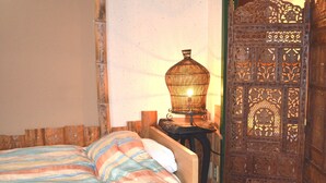 Un llit amb llençols rayats, una taula de nit de fusta i una làmpada decorativa.