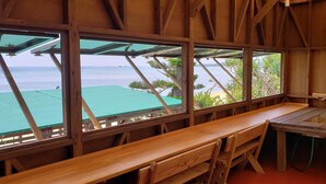 A wooden room with a bench and a table, large windows with a view of the sea and greenery. - Beach Plus (Onna)