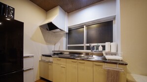 A compact kitchen with a black refrigerator, a stainless steel sink, and a window above the counter. - Beach Plus (Onna)
