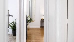 A hallway with white walls and a wooden floor leading to a room with a mirror and a small table. - Live Life Ermou (Athens)